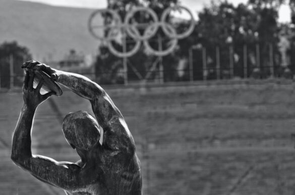 athletic statue in front of olympic rings