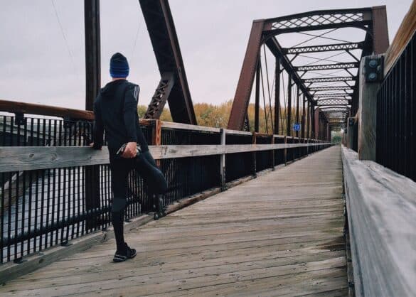 athletic runner stretching on a bridge